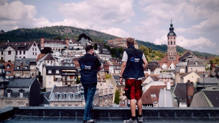 Zwei Mitarbeiter der Firma Zepp stehen auf einem Dach und schauen über Häuserdächer